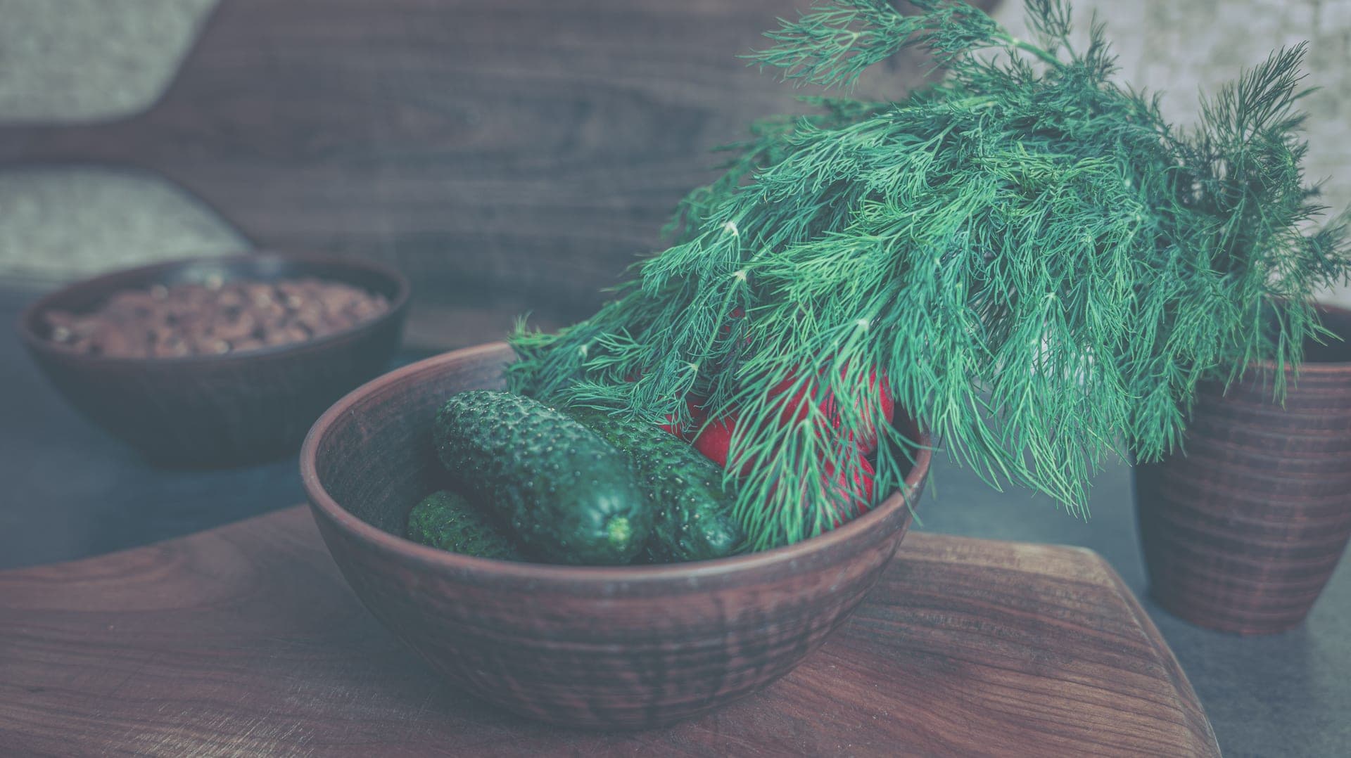 Fresh whole vegetables and herbs arranged on a warm wooden kitchen bench